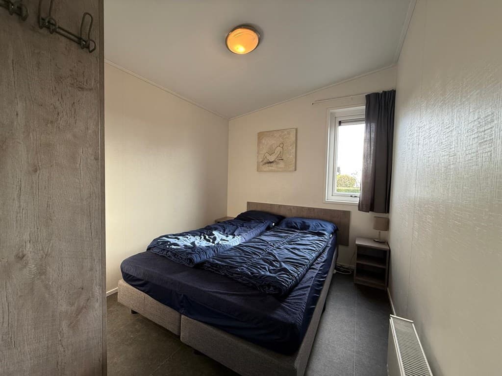 Tweekpersoons slaapkamer met bedden met blauwe dekbedden, een raam en een kunstwerk aan de muur.