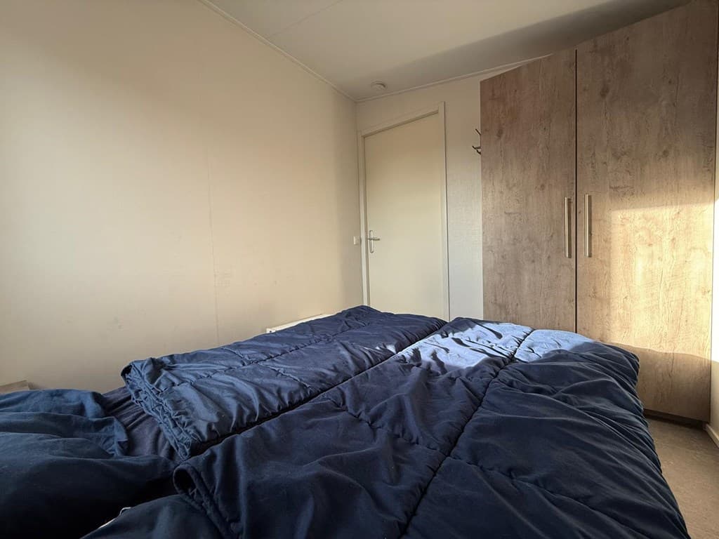 Slaapkamer met twee eenpersoonsbedden en een kast, natuurlijk licht van een raam aan de rechterkant.