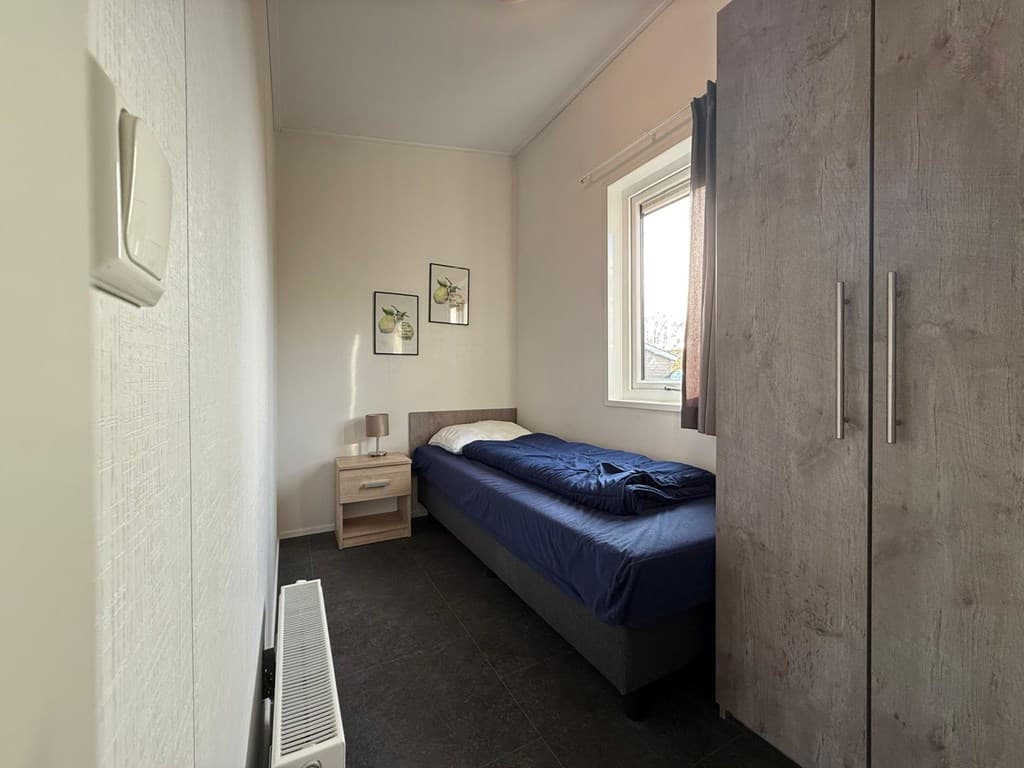 Slaapkamer met een eenpersoonsbed, nachtkastje, kast en een raam met gordijnen.