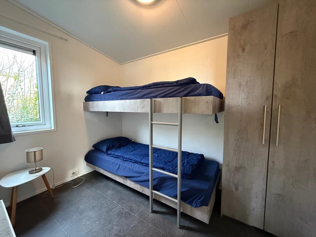 Slaapkamer met een stapelbed en een eenpersoonsbed, een kledingkast en een raam met uitzicht naar buiten