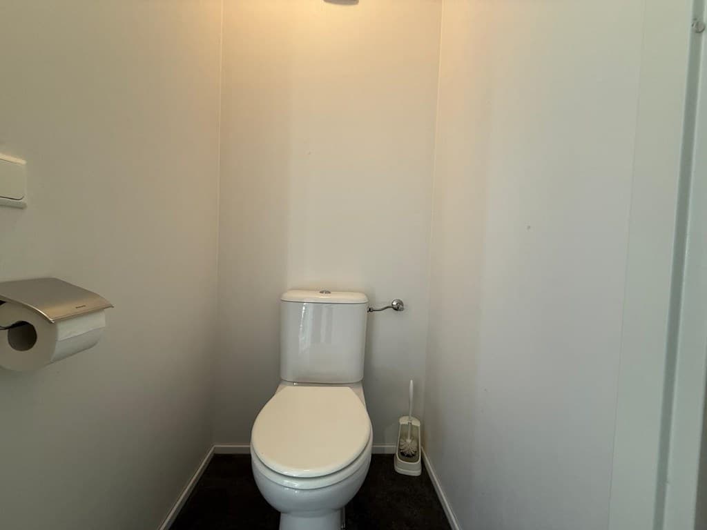 Toilet met witte wand en zwarte vloer, voorzien van een toiletrolhouder en een toiletborstelhouder