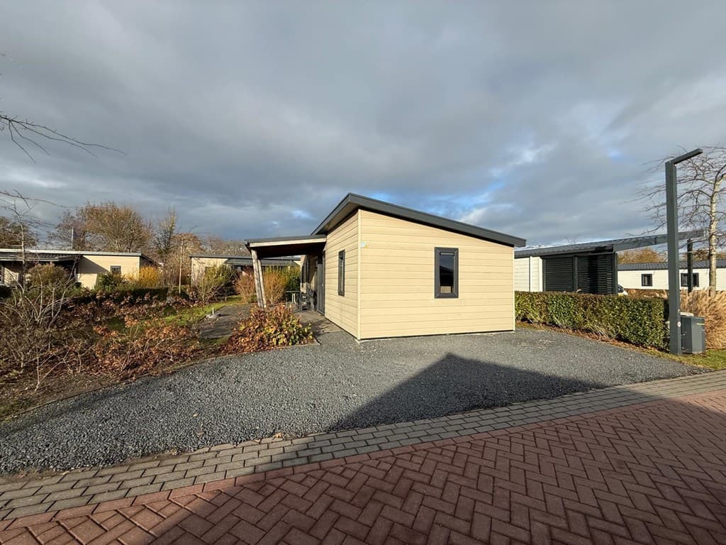 Vakantiehuis aan het EuroParcs Markermeer met een grijze oprit en groene begroeiing rondom, onder een bewolkte lucht
