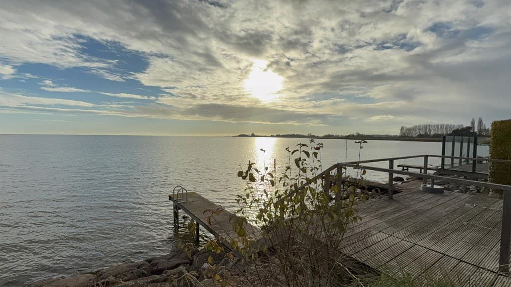Uitzicht op het Markermeer met een houten aanlegsteiger en een zonsondergang aan de horizon met wolken en water.
