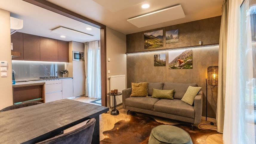 Moderne woonkamer met bank, eettafel en open keuken, voorzien van grote ramen en sfeervolle verlichting
