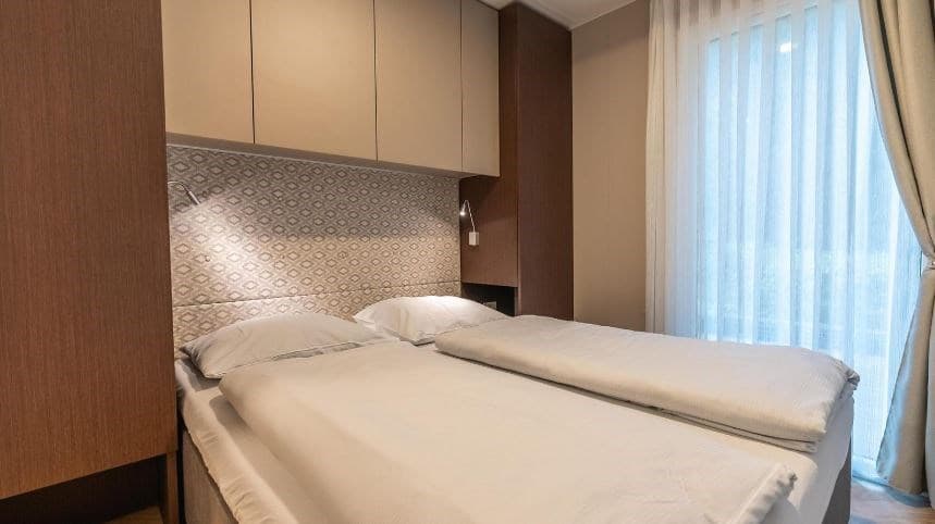 Sfeervolle slaapkamer met twee eenpersoonsbedden en een wand met een decoratieve achterwand en gordijnen.