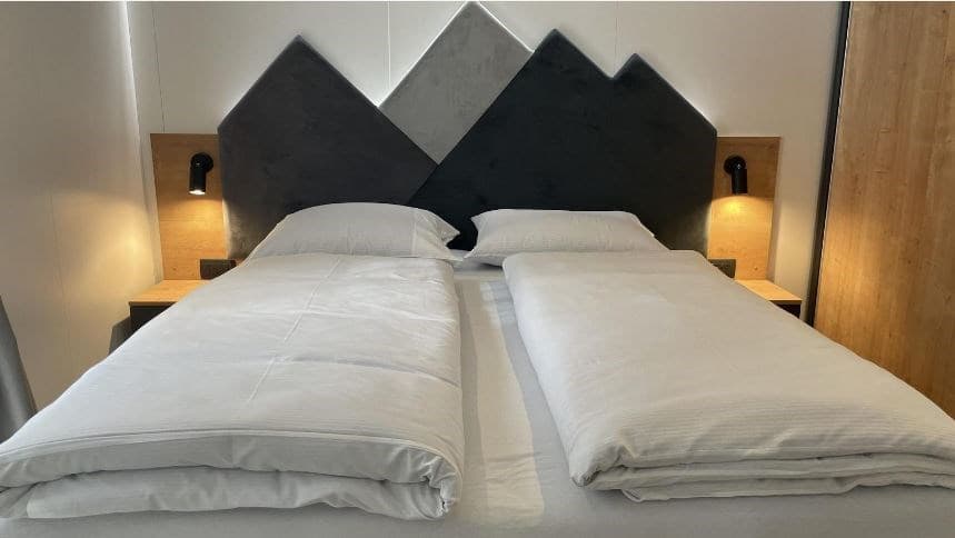 Slaapkamer met een groot bed, nachtkastjes en moderne wandverlichting in een lichte en strakke stijl.