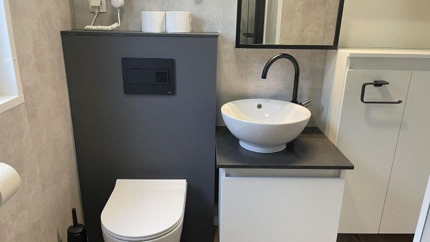 Modern toilet met wastafel en spiegel, grijs wandmeubel en zwarte kraan in een lichte ruimte.