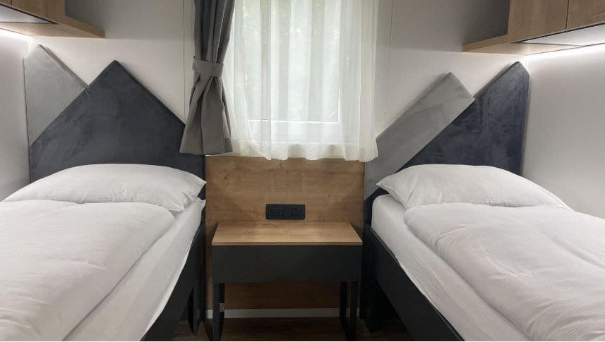 Twee enkele bedden met een nachtkastje ertussen in een moderne slaapkamer met houten accenten en raam met gordijnen