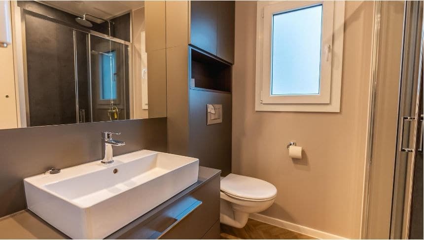 Moderne badkamer met wastafel, toilet en douche in lichte kleuren en natuurlijk licht vanuit het raam.