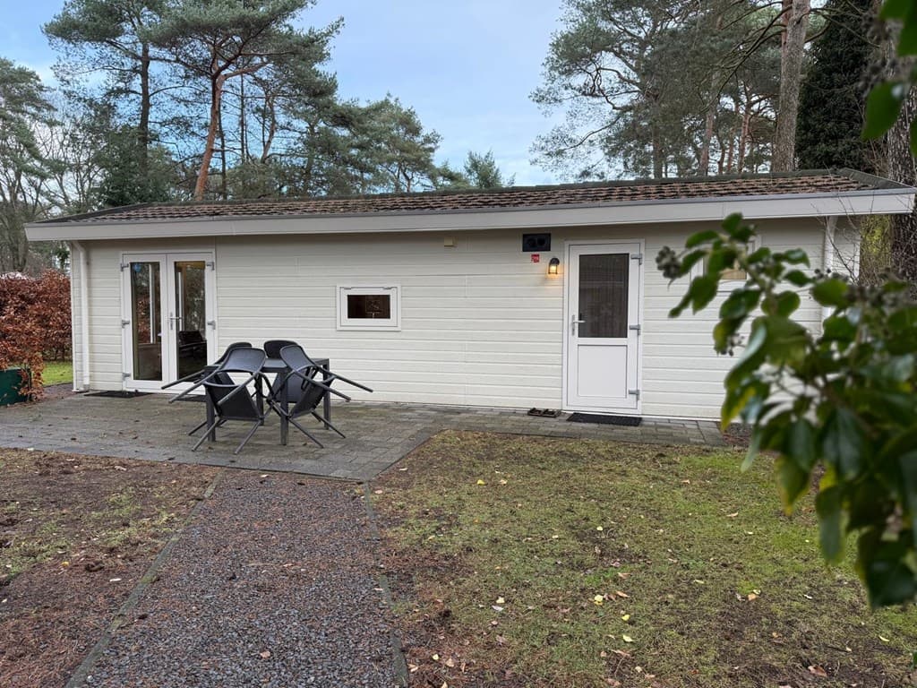 Witte vakantiewoning met een tuin, terras en een set tuinstoelen in een bosrijke omgeving.