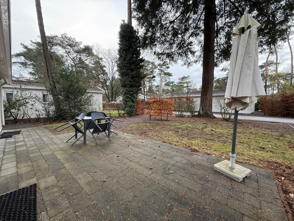 Tuin met terras en tuinmeubelen, omringd door bomen en hagen bij EuroParcs De Zanding in Otterlo