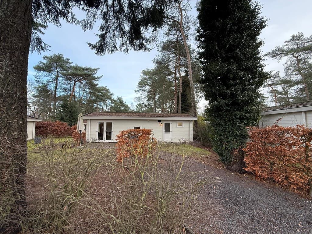 Vakantiewoning omringd door bomen en hagen, met een oprit en glazen deuren aan de voorkant.