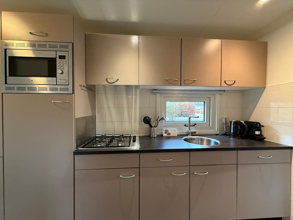Moderne keuken met gasfornuis, oven, spoelbak en elektrische apparaten in neutrale kleuren.