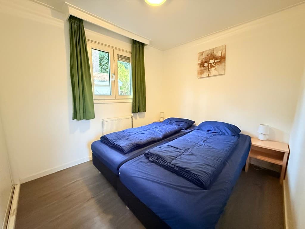 Slaapkamer met twee enkele bedden, een raam met groen gordijn en een nachtkastje met lamp