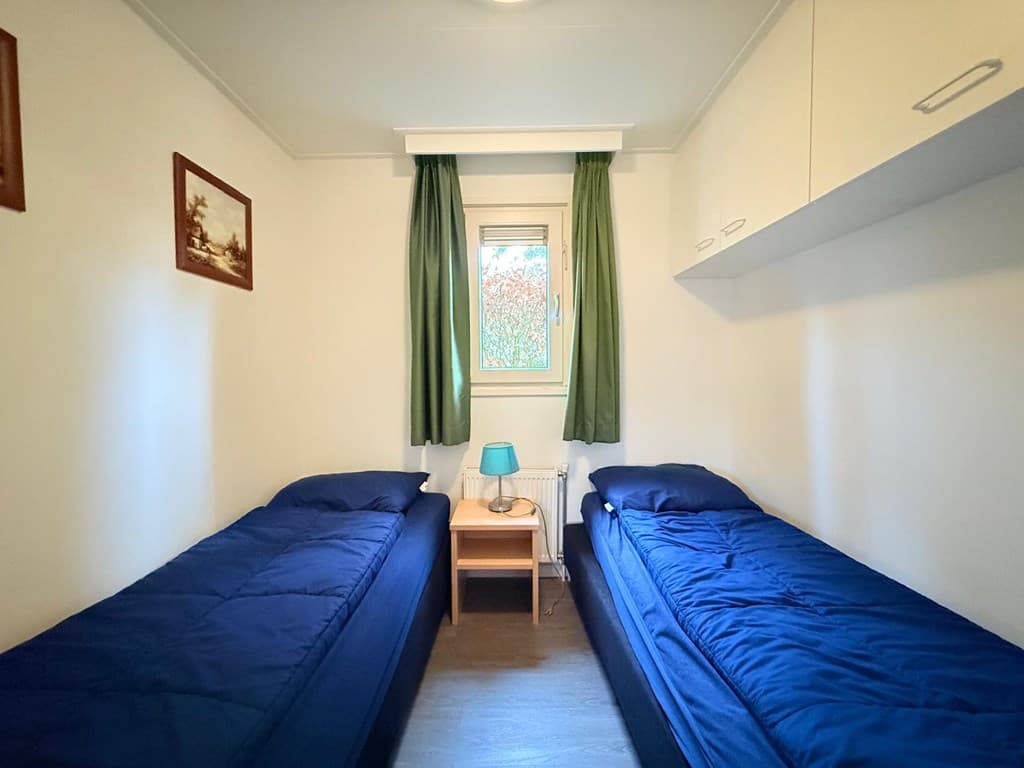 Slaapkamer met twee eenpersoonsbedden, een nachtkastje met een lamp en groene gordijnen bij het raam