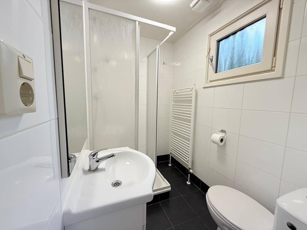 Moderne badkamer met douche, wastafel en toilet, betegelde muren en vloer in witte en zwarte tinten.