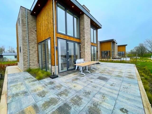 Moderne vakantiewoning met grote glazen deuren en een terras van tegels, omgeven door groen en uitzicht op het landschap