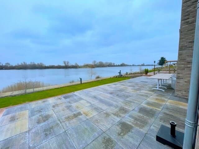 Ruimtelijke terras met uitzicht op de Maas en groene oevervegetatie, onder een bewolkte lucht