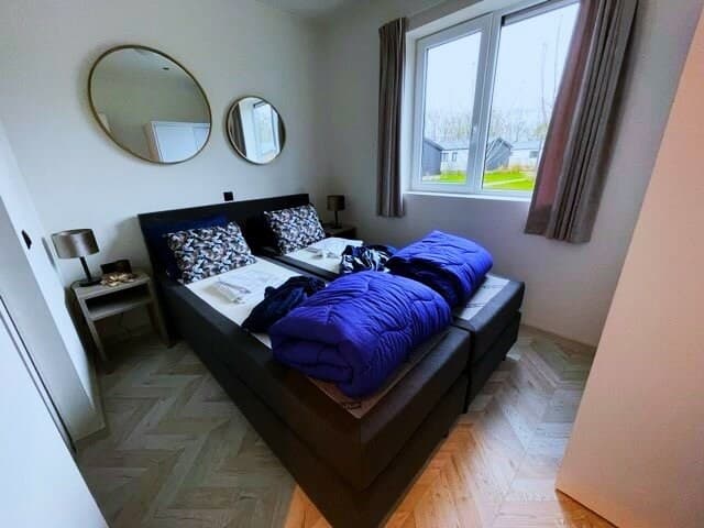 Slaapkamer met twee eenpersoonsbedden, ronde spiegels en ramen met uitzicht op de groene buitenruimte.