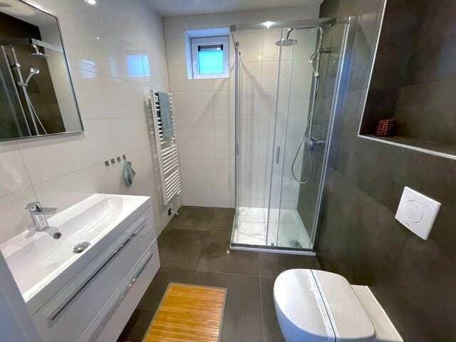 Moderne badkamer met douche, wastafel en toilet, betegeld met witte en donkere tegels.