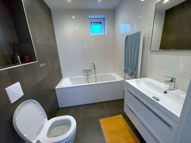 Moderne badkamer met een ligbad, toilet, wastafel en grote spiegel in neutrale kleuren.