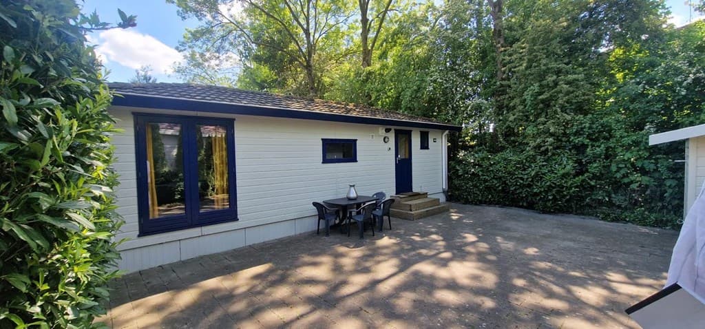 Vakantiehuis met een terras en twee stoelen, omgeven door bomen en groen, gelegen bij Resort Rhederlaagse Meren.