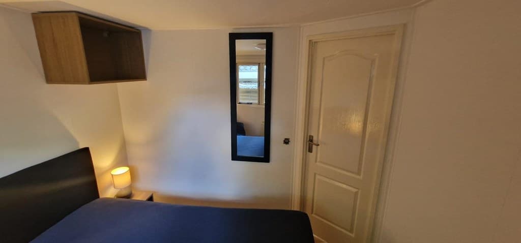 Slaapkamer met een bed, een spiegel, een nachtlampje en een deur naar de gang.