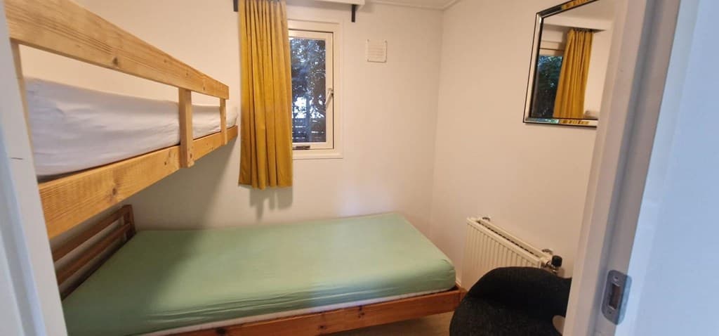 Slaapkamer met stapelbed, een eenpersoonsbed, een raam met gordijnen en een wandspiegel.