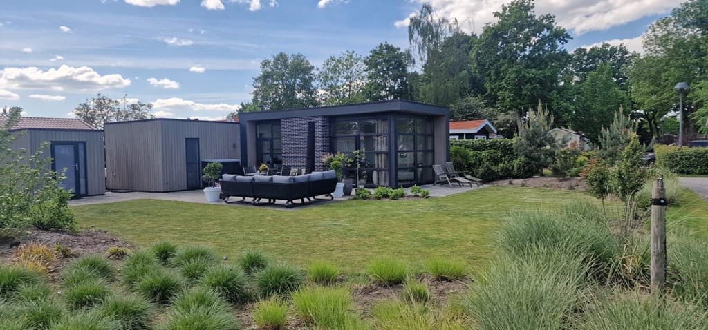Moderne vakantiewoning met ruime tuin, groene grasvelden en zitgedeelte met banken en stoelen, omringd door bomen