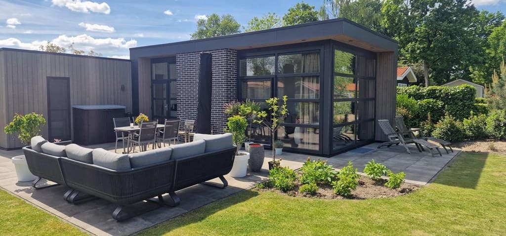 Moderne vakantiewoning met grote ramen, stijlvolle tuinmeubelen en goed onderhouden tuin met groene planten.
