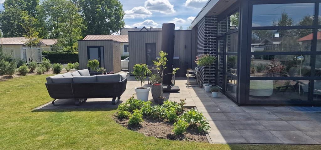 Moderne vakantiewoning met terras, zithoek en groene tuin bij EuroParcs Bad Hoophuizen, omgeven door bomen en andere woningen