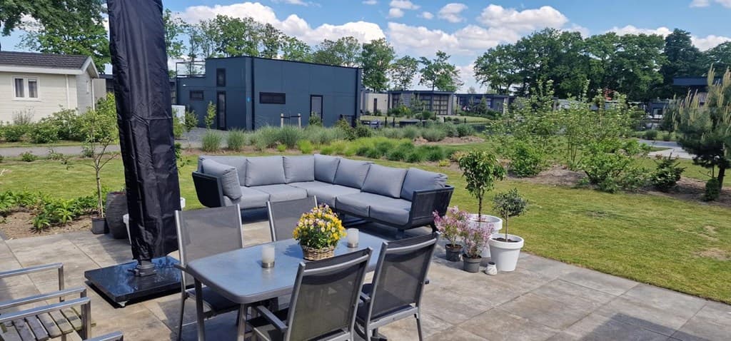 Terras met een zithoek en eettafel, omringd door groen en andere woningen in de achtergrond