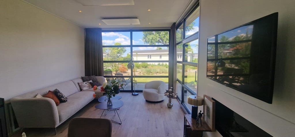 Lichte woonkamer met grote ramen, moderne inrichting en uitzicht op de tuin en omgeving van EuroParcs Bad Hoophuizen.