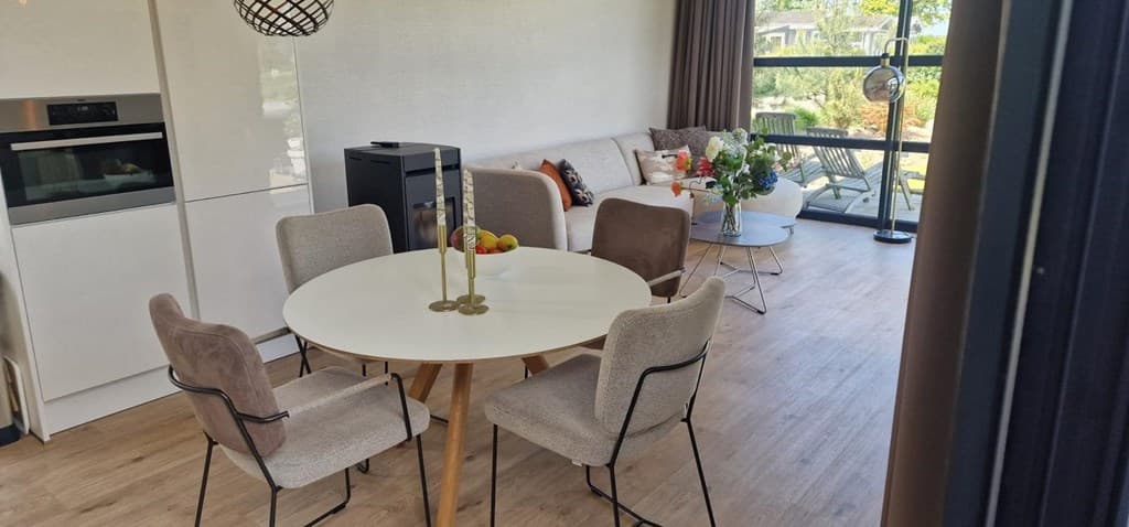 Eetkamer met ronde tafel en stoelen, moderne inrichting en zithoek met grote ramen voor natuurlijk licht.