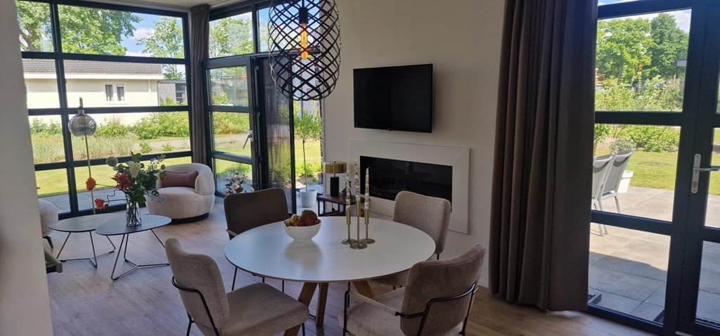 Woonruimte met eettafel, stoelen, modern meubel en grote ramen met uitzicht op de tuin en buitenruimte