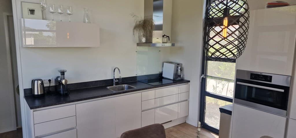 Keuken met moderne meubels, zwarte aanrecht, koelkast, oven en veel lichtinval door grote ramen