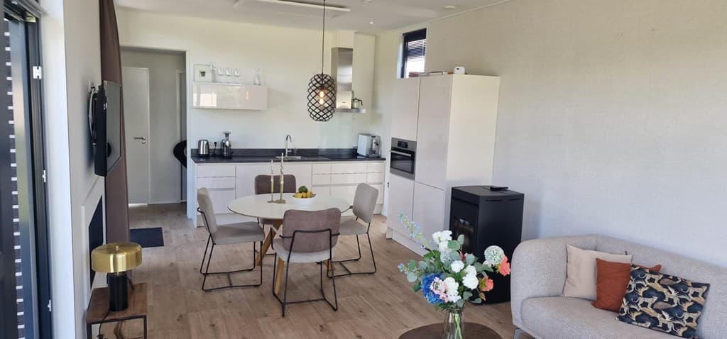 Moderne woonkamer met keuken, ronde eettafel en zithoek met bank, voorzien van plant en decoratieve kussens