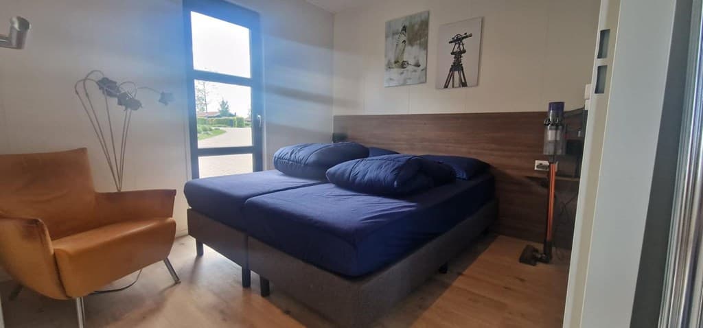 Slaapkamer met twee aparte bedden, een comfortabele stoel en een raam met uitzicht op de buitenruimte