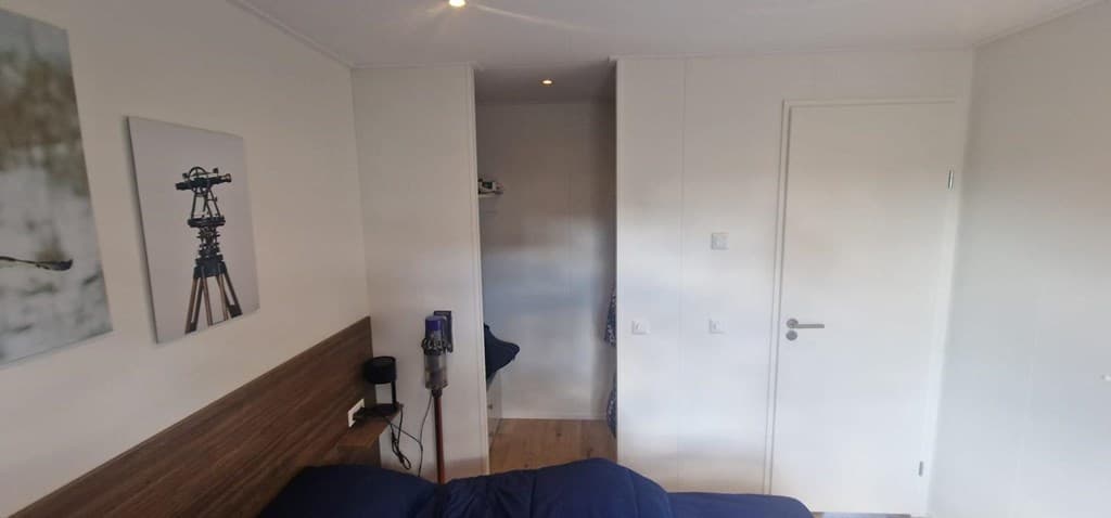 Slaapkamer met bed, een schilderij aan de muur en zicht op een gang met kledingkast.