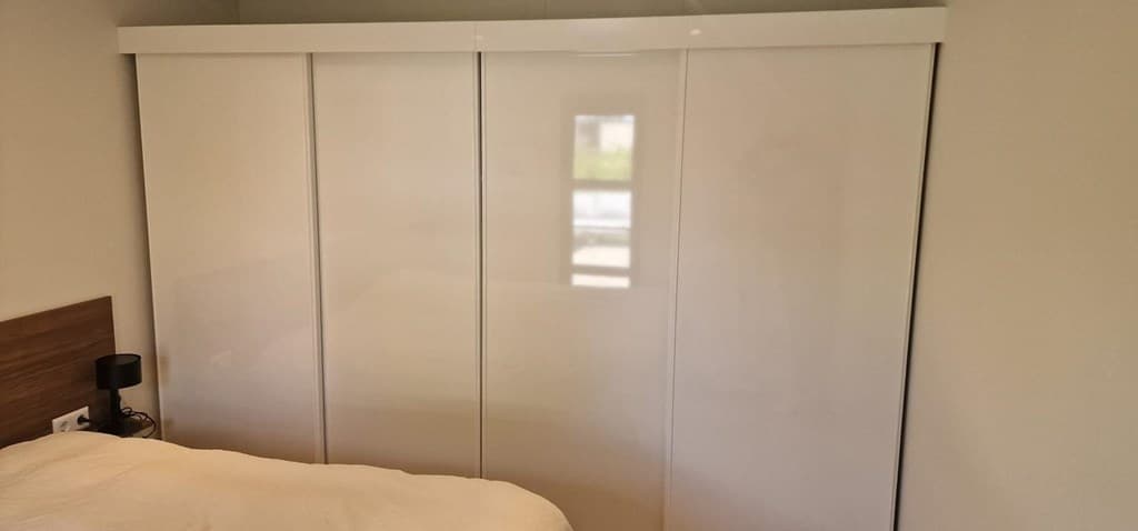 Inbouwkast met witte deuren naast een bed in een lichte slaapkamer