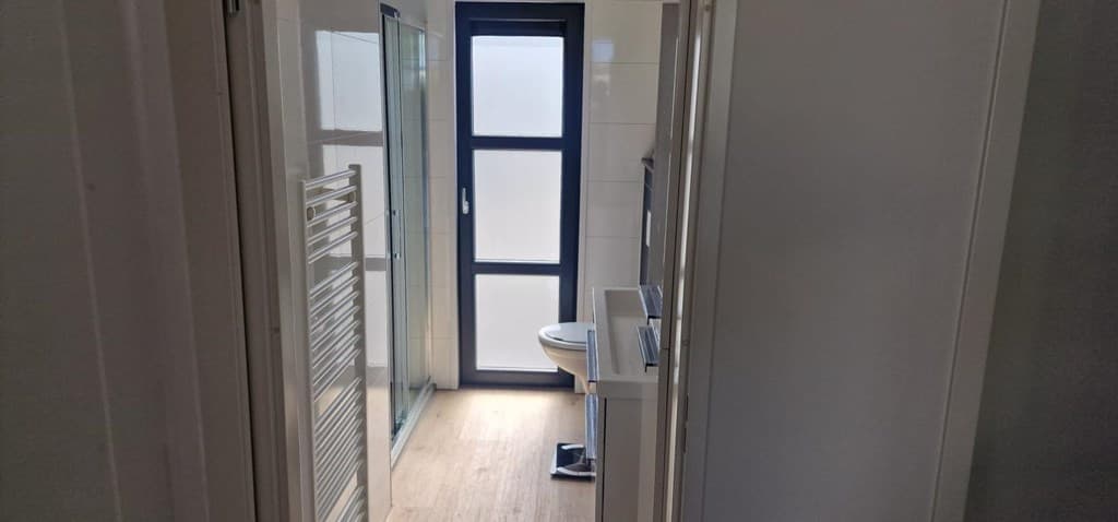 Moderne badkamer met glazen douche, toilet en uitzicht op een raam met matglas.