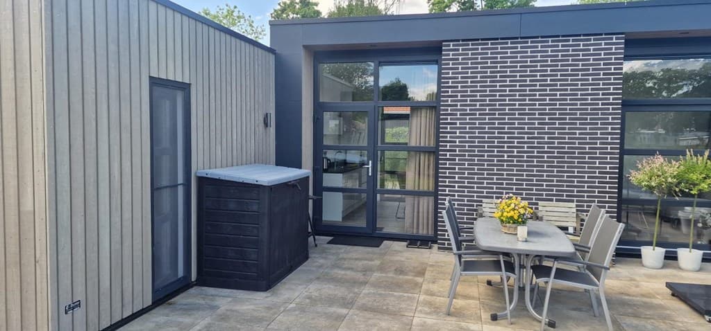 Terras met tegelvloer, houten meubels en een schuur, omlijst door moderne gevels van hout en steen.