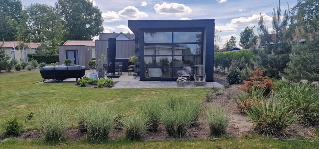 Moderne vakantiewoning met een tuin en zithoek, omringd door groene hagen en diverse planten.