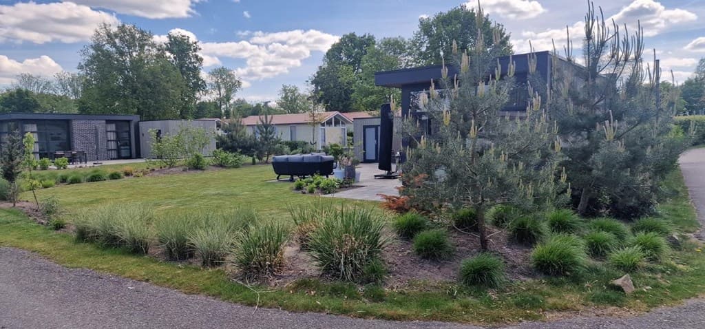 Tuin met grasveld, planten en struiken rondom een moderne woning, zichtbaar vanaf een verhard pad.