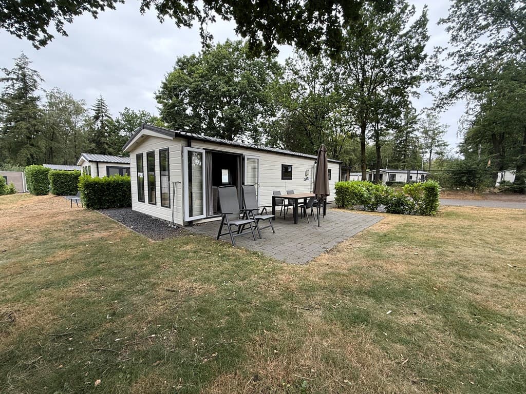 Vakantiehuis met terras en tuin, omringd door bomen en gras in een rustige omgeving.