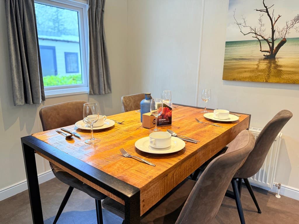 Eetkamer met een houten tafel en vier stoelen, gedekt met servies en glazen, tegen een muur met een schilderij