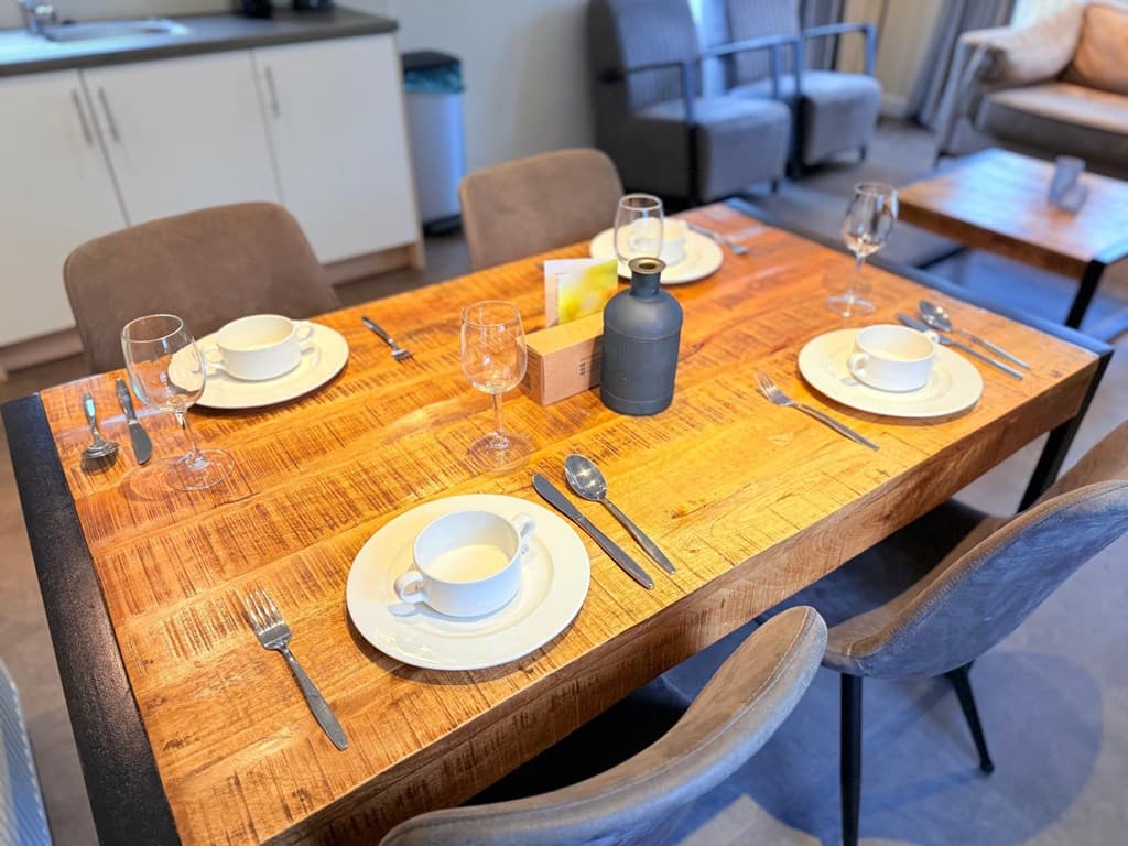 Eettafel met gedekte tafel en glazen, gelegen in een woonkamer met moderne stoelen en keukenkastjes op de achtergrond