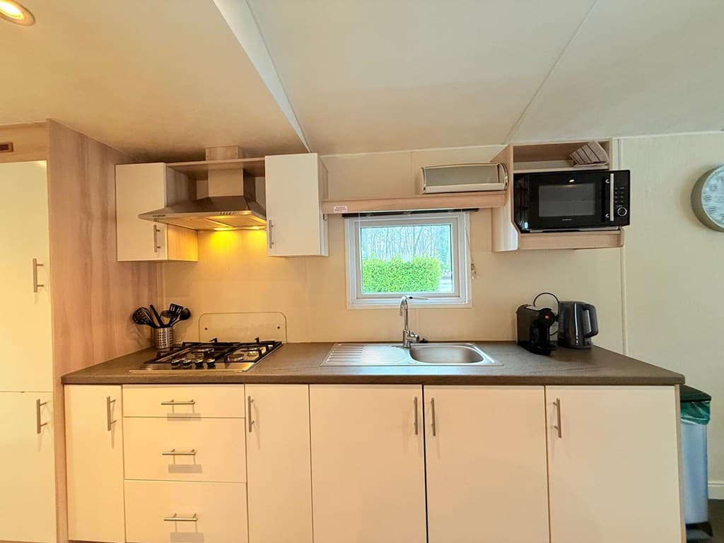 Moderne keuken met gaskookplaat, oven, spoelbak en magnetron in lichte kleuren en venster met uitzicht op buiten.