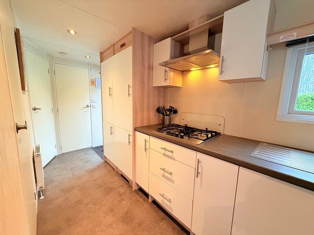 Witte keuken met moderne kasten, gasfornuis en afzuigkap, zichtbaar aan de rechterkant van de foto.