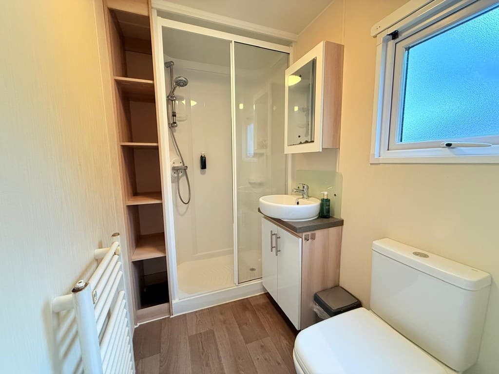 Moderne badkamer met inloopdouche, wastafel en toilet, lichtinval door raam en houten vloer.